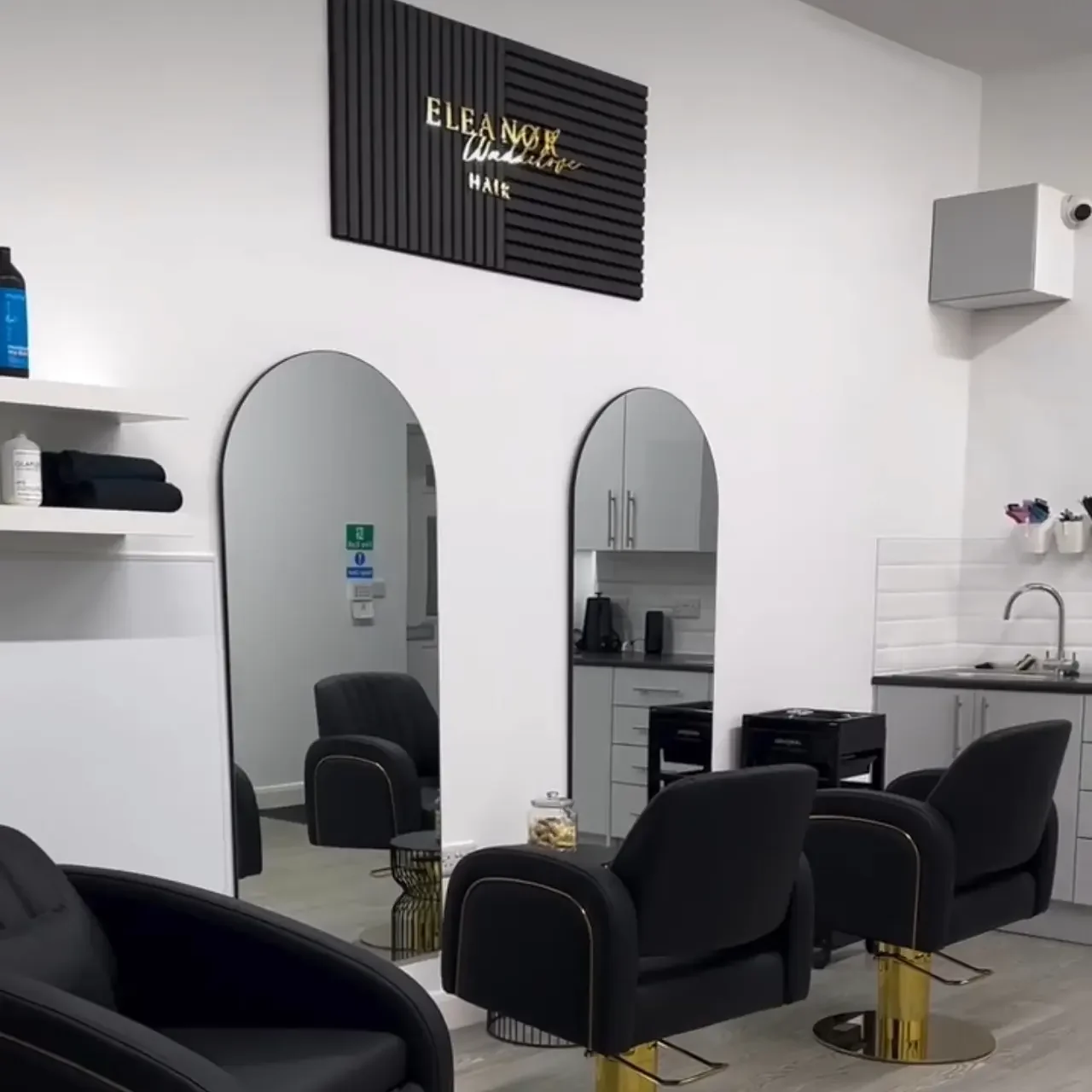 Inside the Eleanor Waddilove Hair salon in Oswaldtwistle: branded sign, black and gold styling chairs, calm white interior